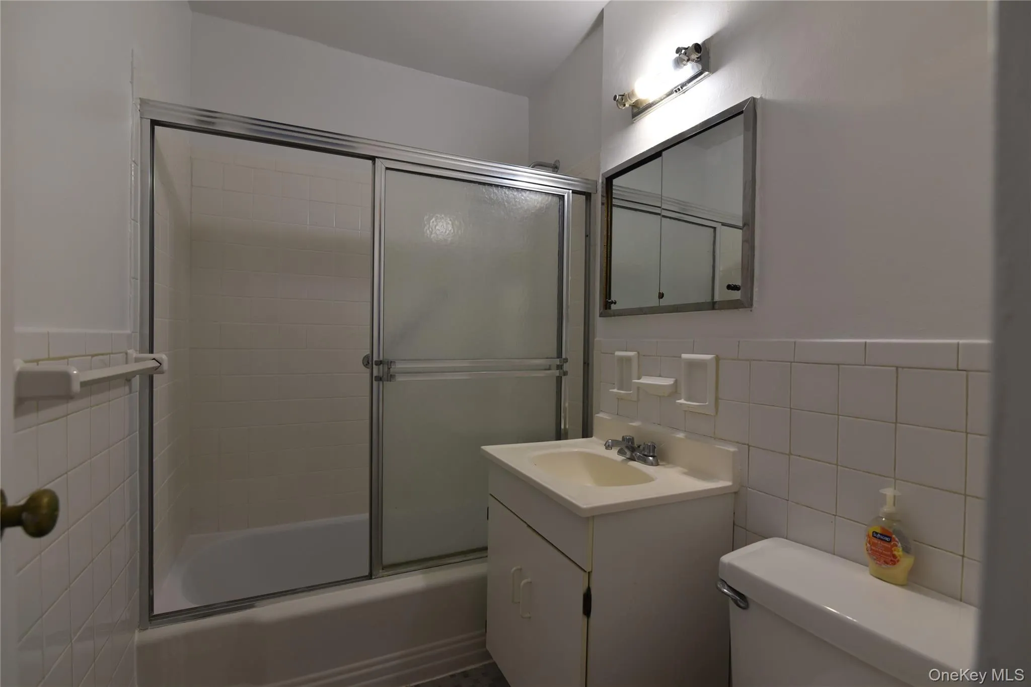 Bathroom featuring tile walls, vanity, shower / bath combination with glass door, and a wainscoted wall Bathroom featuring tile walls, vanity, shower / bath combination with glass door, and a wainscoted wall