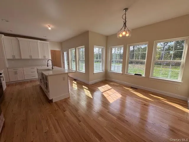 Kitchen featuring an island with sink, white cabinetry, hanging light fixtures, light wood finished floors, and a chandelier Kitchen featuring an island with sink, white cabinetry, hanging light fixtures, light wood finished floors, and a chandelier