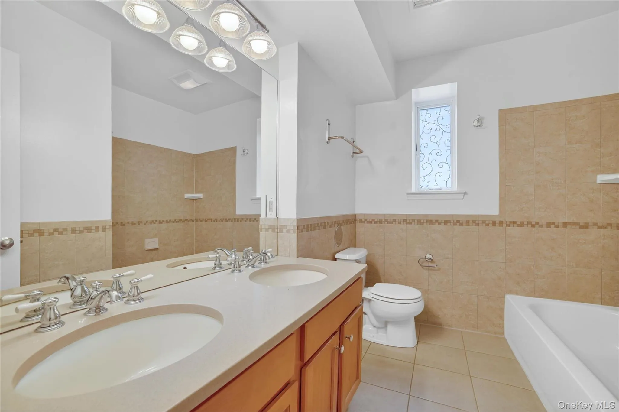 Bathroom with tile walls, double vanity, light tile patterned flooring, and a tile walls. Bathroom with tile walls, double vanity, light tile patterned flooring, and a tile walls.