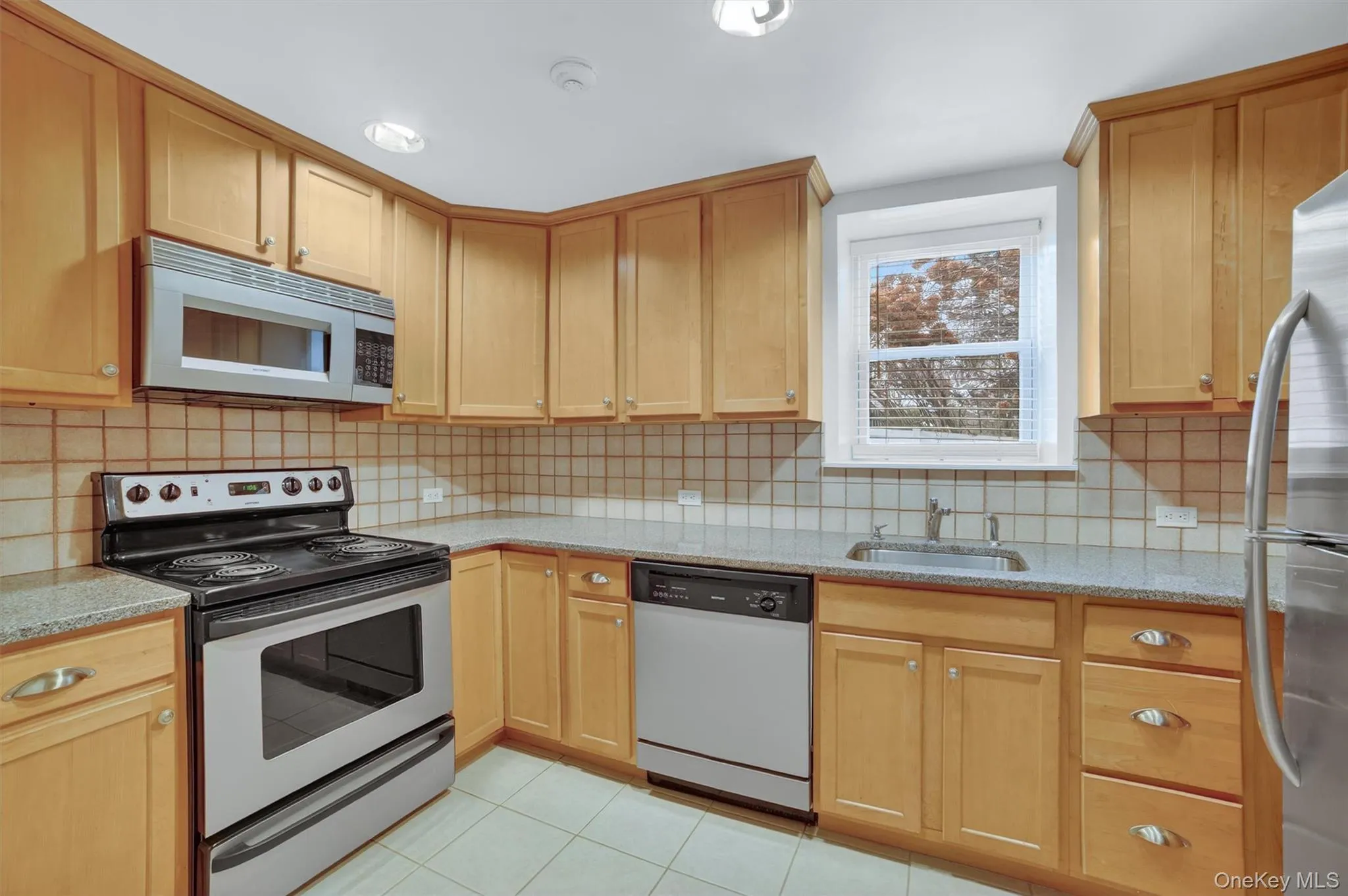 Kitchen with appliances with stainless steel finishes, granite counters, tasteful backsplash, and light tile patterned floors Kitchen with appliances with stainless steel finishes, granite counters, tasteful backsplash, and light tile patterned floors