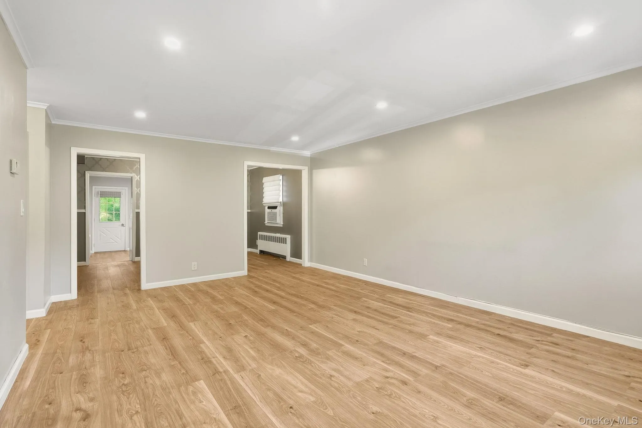 Empty room with ornamental molding, recessed lighting, radiator, and light wood finished floors Empty room with ornamental molding, recessed lighting, radiator, and light wood finished floors