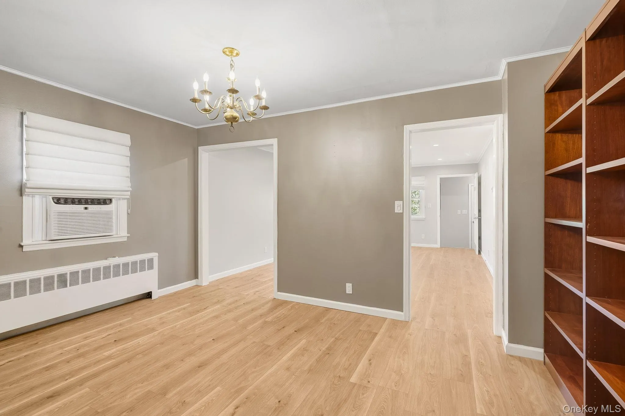 Unfurnished dining area with light wood finished floors, a chandelier, crown molding, cooling unit, and radiator heating unit Unfurnished dining area with light wood finished floors, a chandelier, crown molding, cooling unit, and radiator heating unit