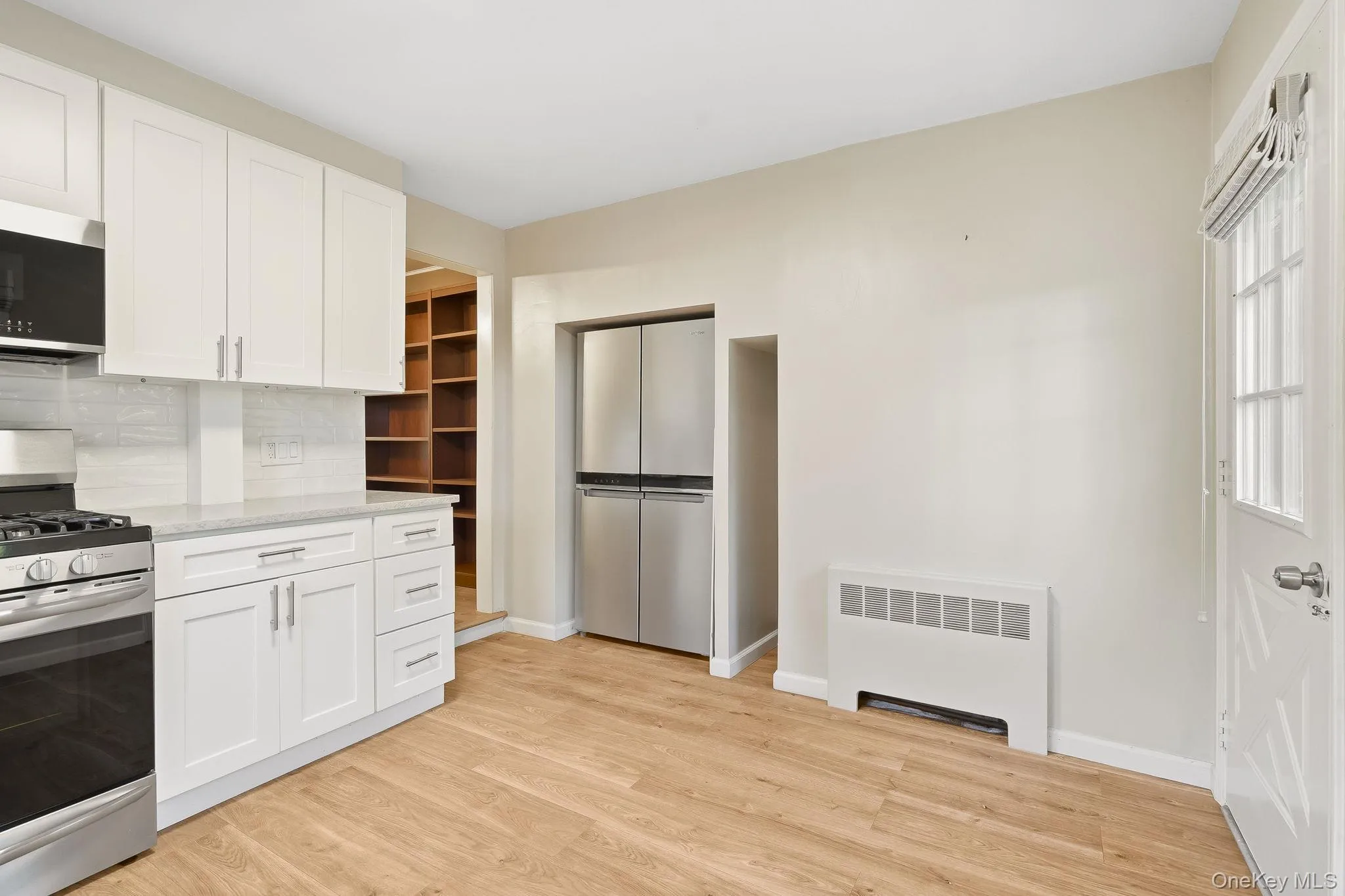 Kitchen with stainless steel appliances, radiator heating unit, white cabinetry, and light stone countertops Kitchen with stainless steel appliances, radiator heating unit, white cabinetry, and light stone countertops