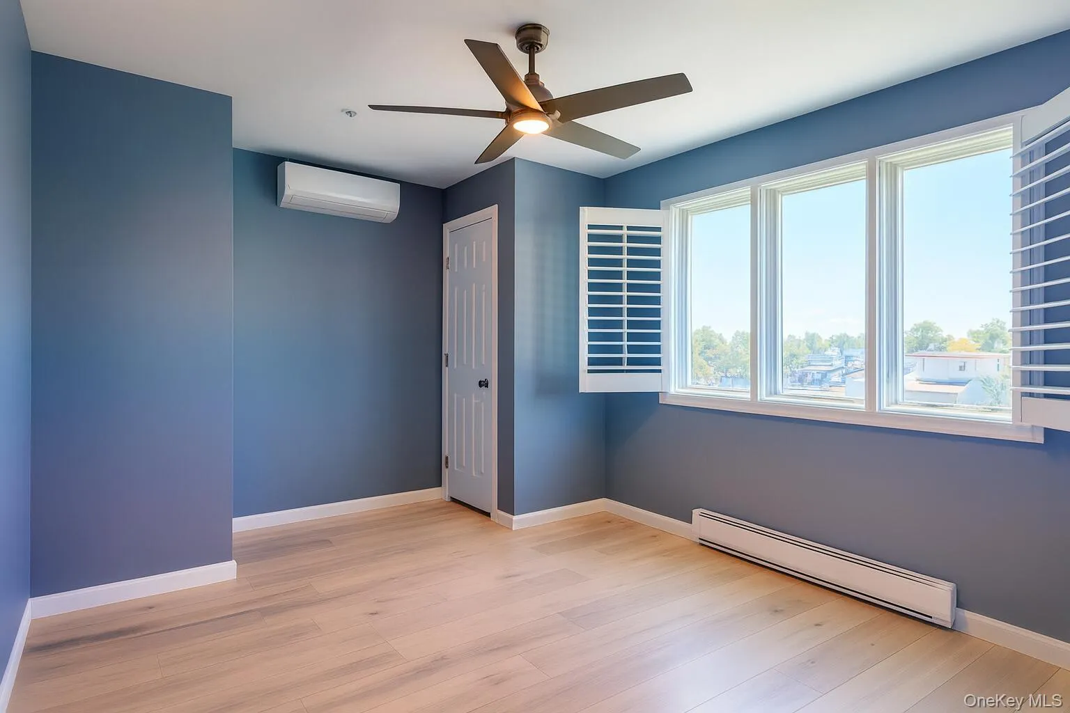 Spare room featuring a baseboard radiator, light wood finished floors, a wall mounted air conditioner, and a ceiling fan Spare room featuring a baseboard radiator, light wood finished floors, a wall mounted air conditioner, and a ceiling fan