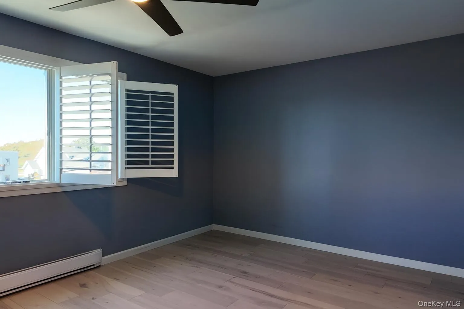 Unfurnished room with a baseboard radiator, light wood finished floors, and ceiling fan Unfurnished room with a baseboard radiator, light wood finished floors, and ceiling fan