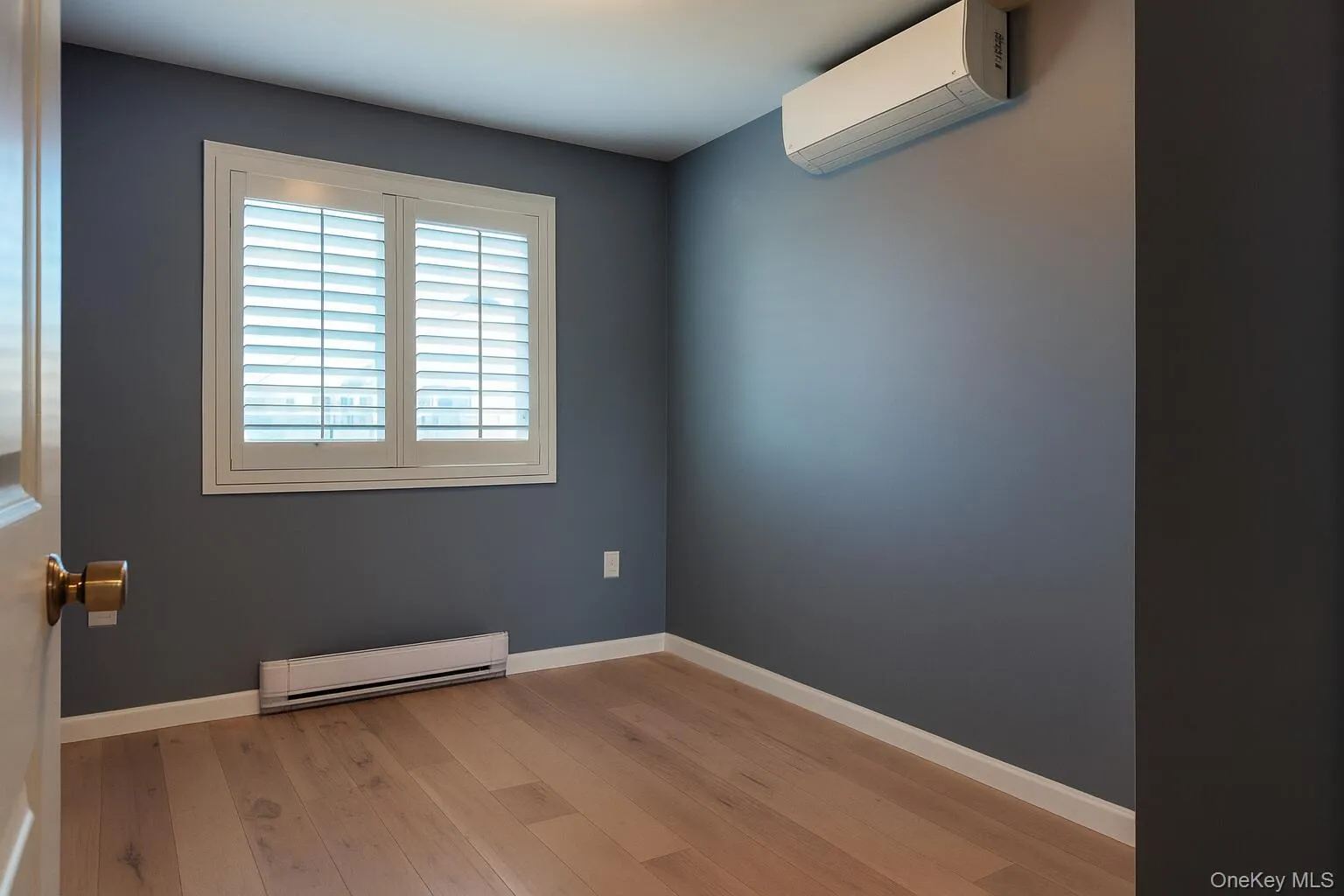 Unfurnished room featuring baseboard heating, a wall unit AC, and light wood-style flooring Unfurnished room featuring baseboard heating, a wall unit AC, and light wood-style flooring