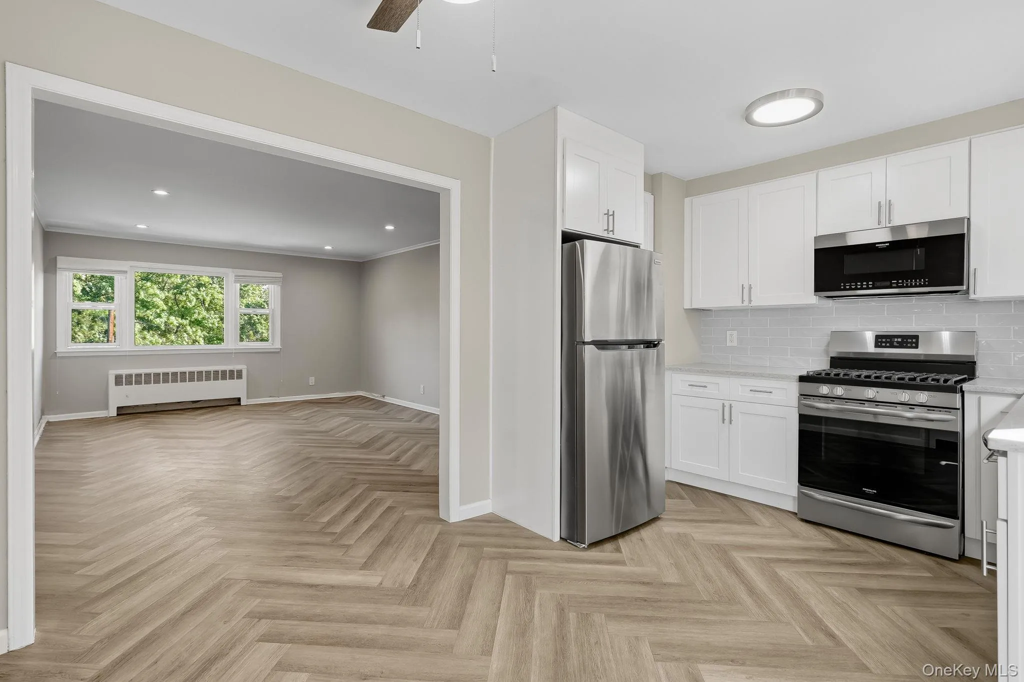 Kitchen featuring appliances with stainless steel finishes, backsplash, white cabinets, radiator heating unit, and recessed lighting Kitchen featuring appliances with stainless steel finishes, backsplash, white cabinets, radiator heating unit, and recessed lighting