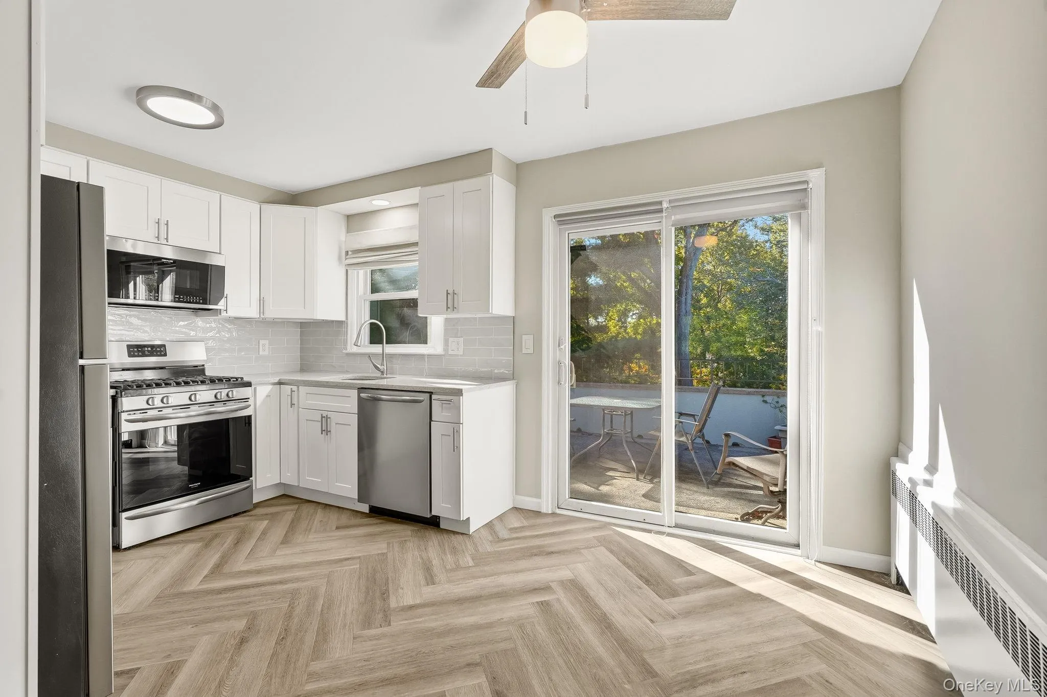Kitchen featuring radiator, appliances with stainless steel finishes, decorative backsplash, white cabinets, and ceiling fan Kitchen featuring radiator, appliances with stainless steel finishes, decorative backsplash, white cabinets, and ceiling fan