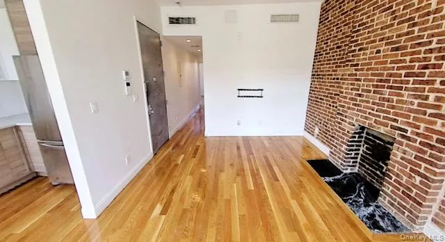 Unfurnished living room featuring a fireplace, light wood-type flooring, and brick wall Unfurnished living room featuring a fireplace, light wood-type flooring, and brick wall