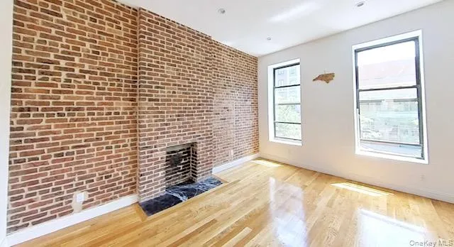 Unfurnished living room featuring brick wall, light wood finished floors, and a large fireplace Unfurnished living room featuring brick wall, light wood finished floors, and a large fireplace