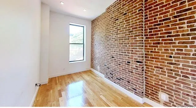 Unfurnished room with light wood-type flooring, brick wall, and recessed lighting Unfurnished room with light wood-type flooring, brick wall, and recessed lighting