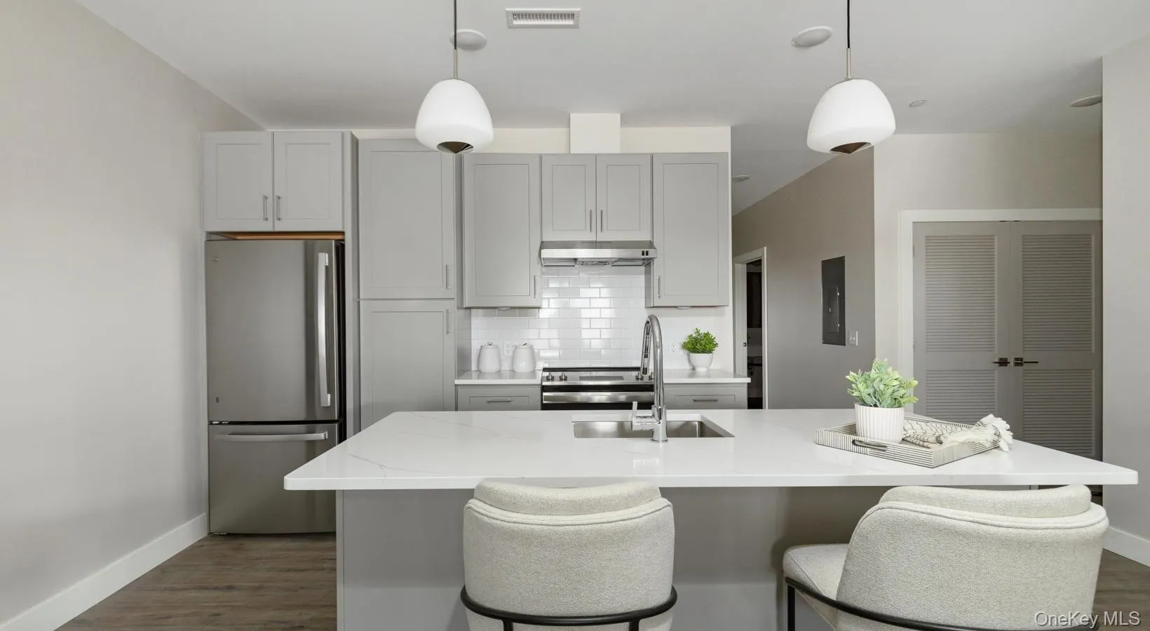 Kitchen featuring appliances with stainless steel finishes, decorative backsplash, hanging light fixtures, dark wood finished floors, and light stone counters Kitchen featuring appliances with stainless steel finishes, decorative backsplash, hanging light fixtures, dark wood finished floors, and light stone counters