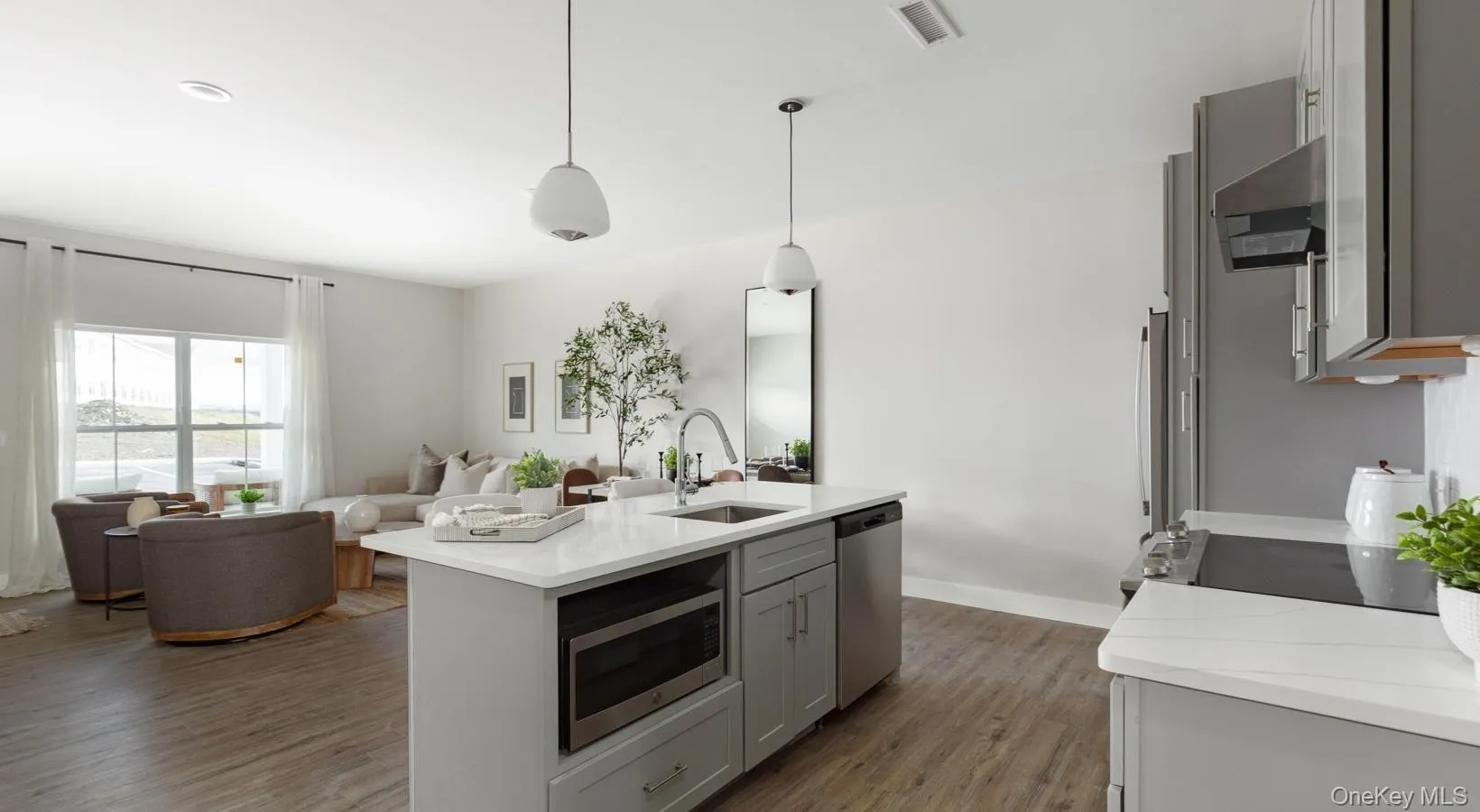 Kitchen with wood finished floors, gray cabinets, exhaust hood, open floor plan, and stainless steel appliances Kitchen with wood finished floors, gray cabinets, exhaust hood, open floor plan, and stainless steel appliances