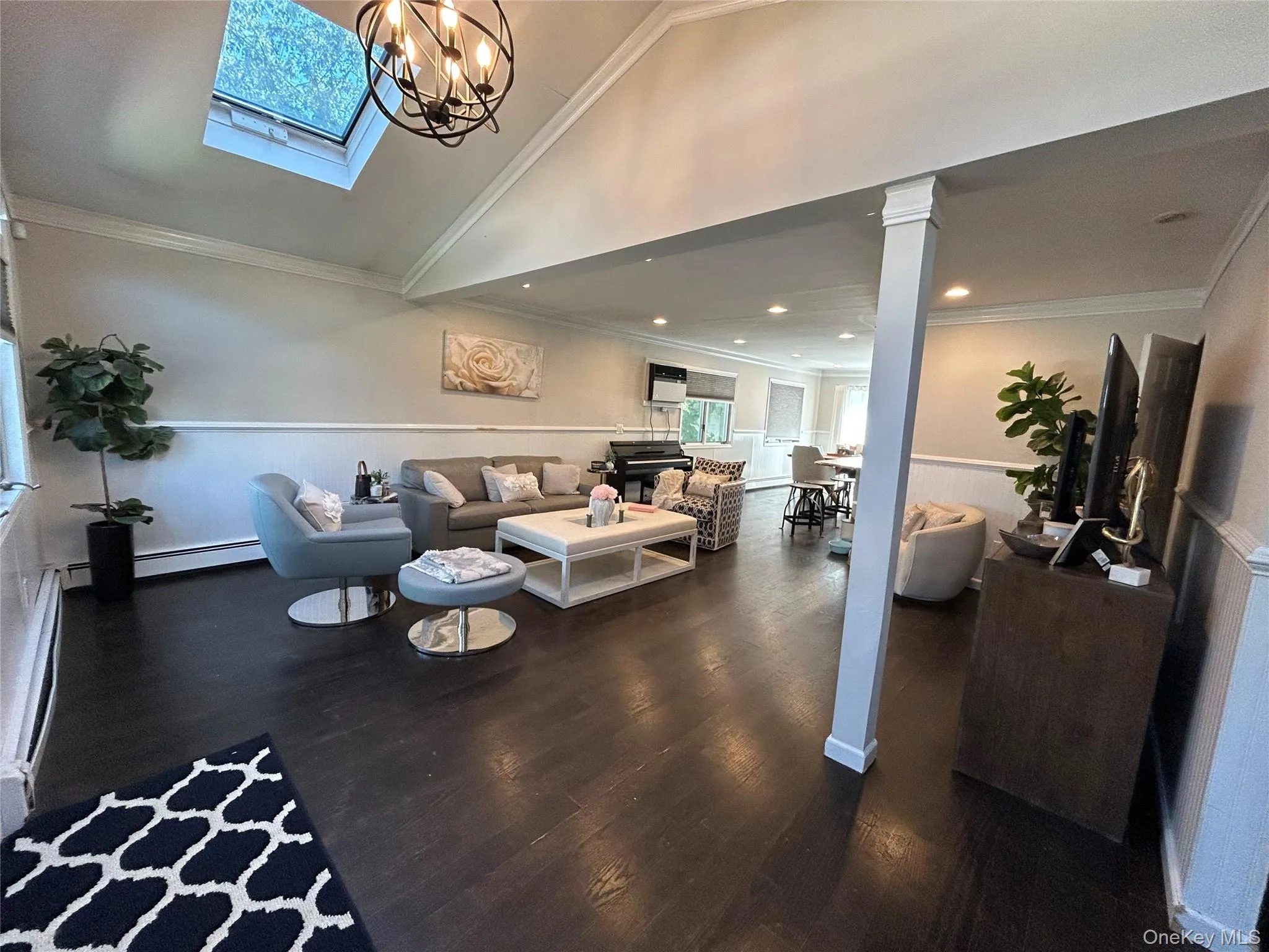 Living room with wainscoting, ornamental molding, dark wood-type flooring, a baseboard radiator, and a chandelier Living room with wainscoting, ornamental molding, dark wood-type flooring, a baseboard radiator, and a chandelier