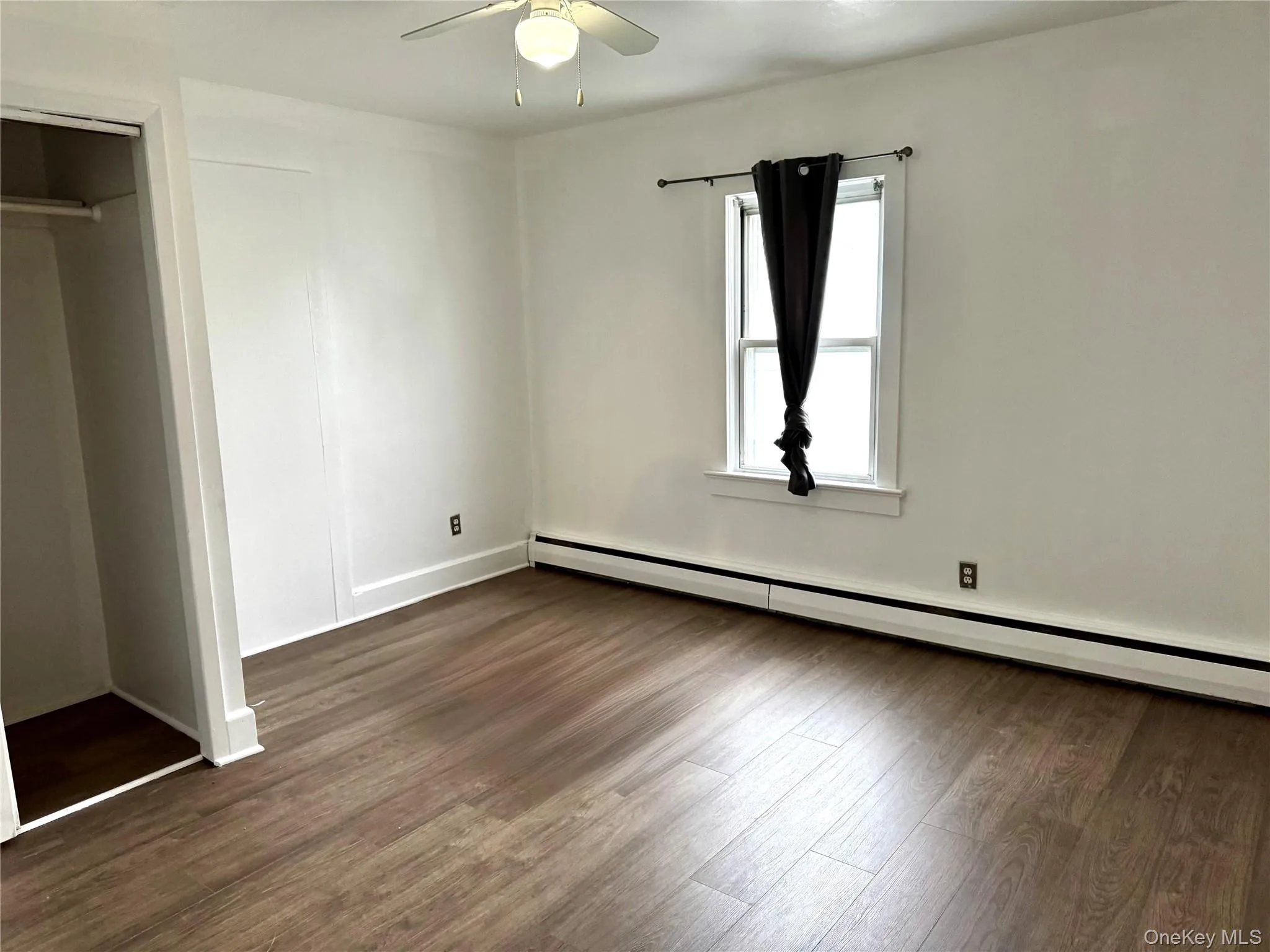 bedroom featuring a baseboard heating unit, dark wood-style floors, ceiling fan, and a closet bedroom featuring a baseboard heating unit, dark wood-style floors, ceiling fan, and a closet