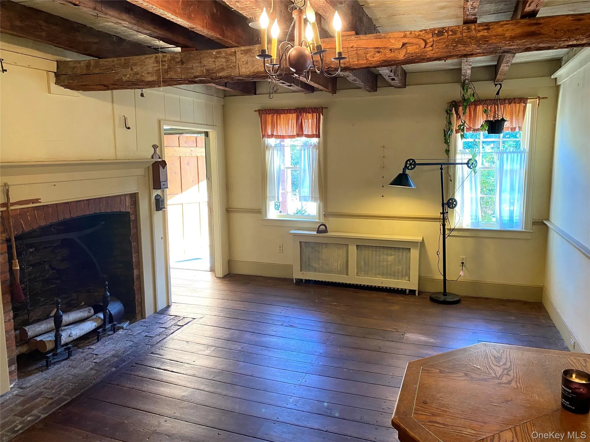 Unfurnished living room with beam ceiling, radiator, hardwood / wood-style flooring, and a chandelier Unfurnished living room with beam ceiling, radiator, hardwood / wood-style flooring, and a chandelier