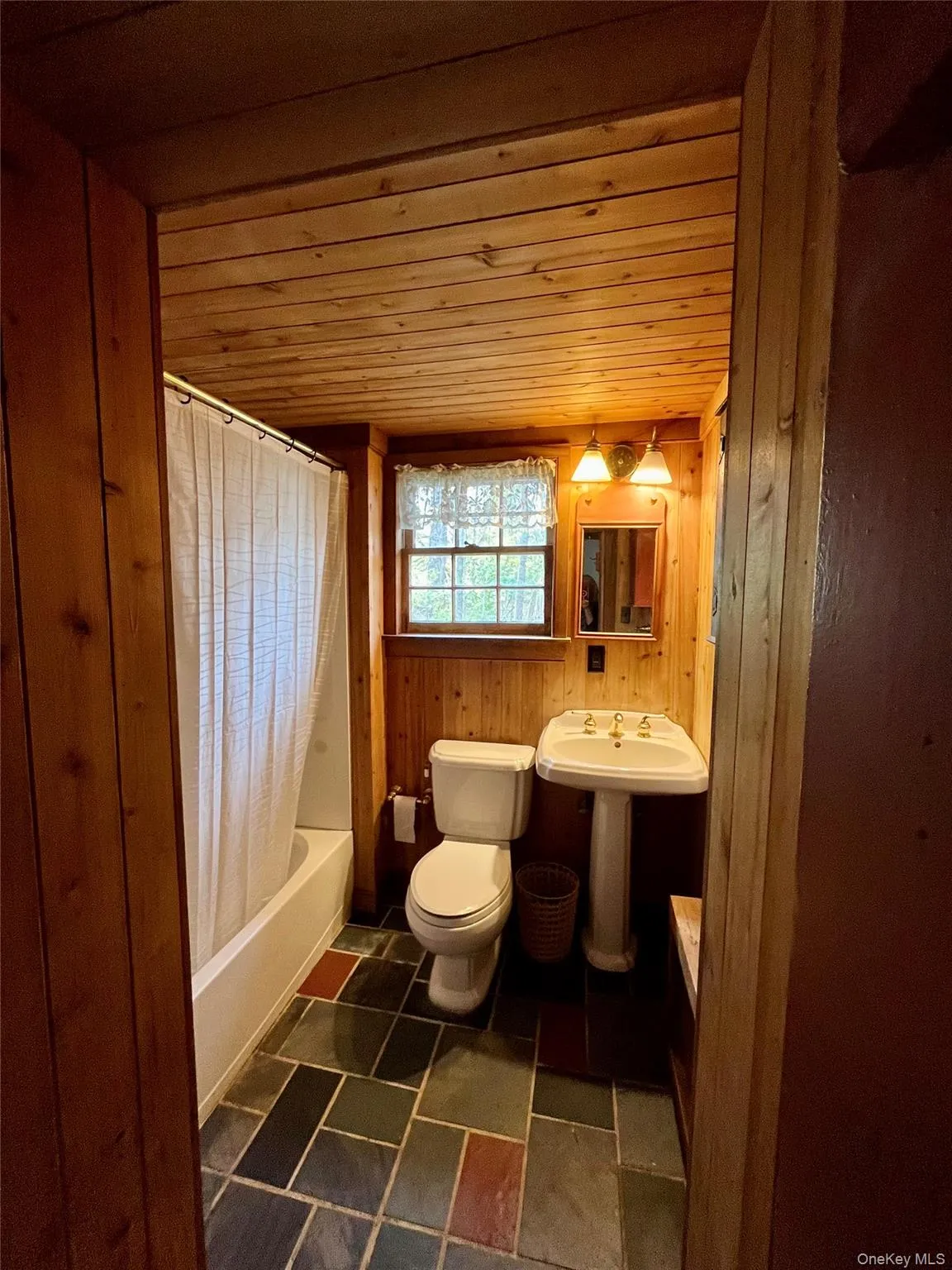 Bathroom featuring wood walls, shower / bathtub combination with curtain, and wooden ceiling Bathroom featuring wood walls, shower / bathtub combination with curtain, and wooden ceiling