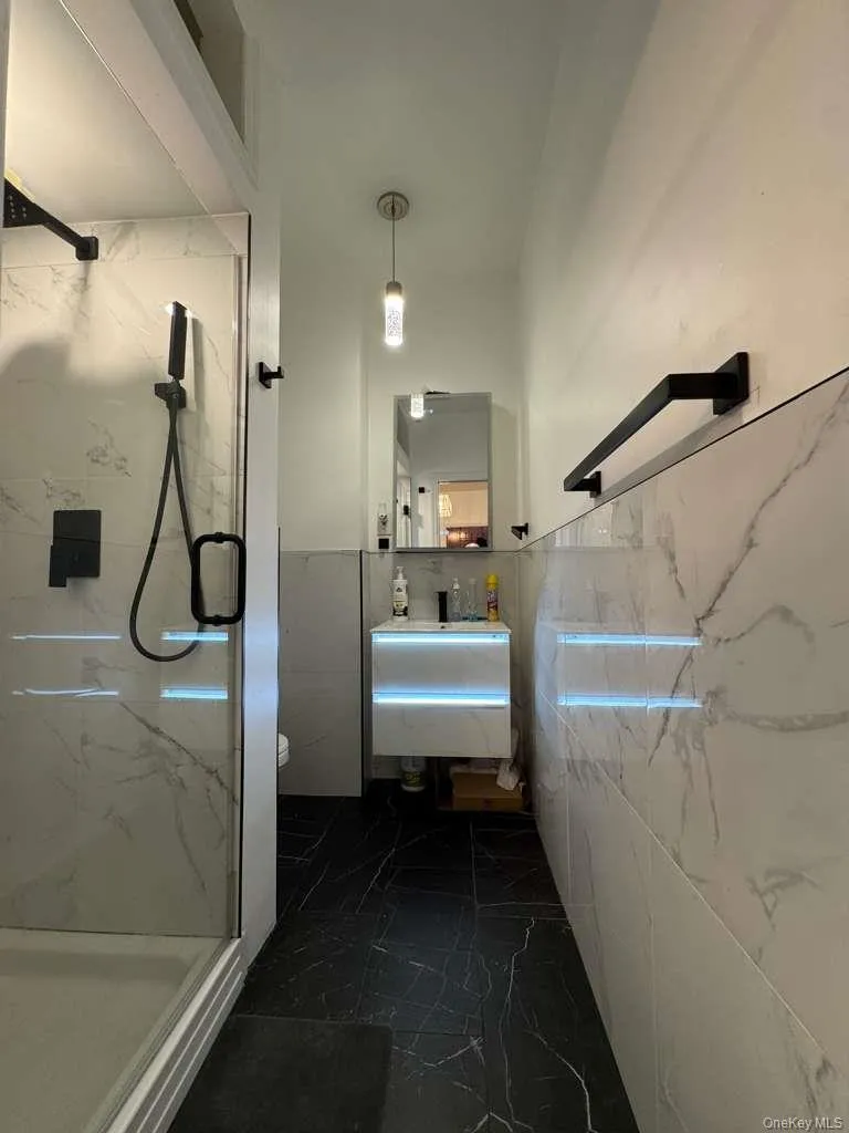 Full bath with a marble finish shower, dark marble finish floors, tile walls, and a wainscoted wall Full bath with a marble finish shower, dark marble finish floors, tile walls, and a wainscoted wall