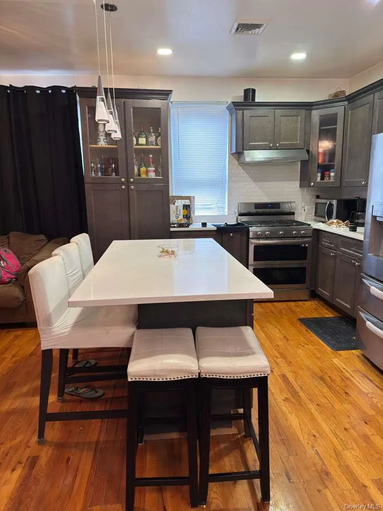 Kitchen featuring glass insert cabinets, a kitchen bar, appliances with stainless steel finishes, dark brown cabinets, and recessed lighting Kitchen featuring glass insert cabinets, a kitchen bar, appliances with stainless steel finishes, dark brown cabinets, and recessed lighting