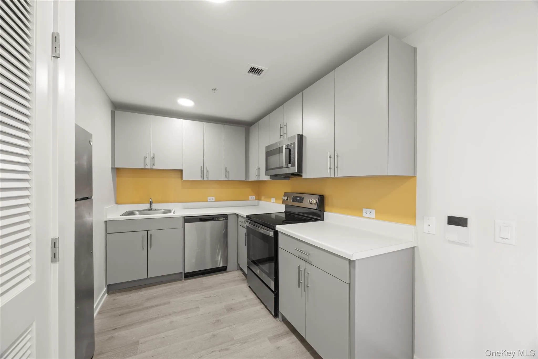 Kitchen featuring gray cabinets, appliances with stainless steel finishes, light countertops, light wood-style floors, and recessed lighting Kitchen featuring gray cabinets, appliances with stainless steel finishes, light countertops, light wood-style floors, and recessed lighting