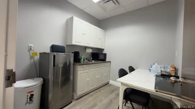Kitchen with a drop ceiling, freestanding refrigerator, light wood-style floors, white cabinets, and black microwave Kitchen with a drop ceiling, freestanding refrigerator, light wood-style floors, white cabinets, and black microwave