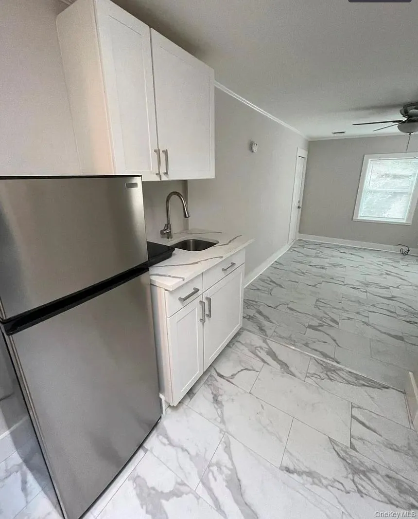 Kitchen with freestanding refrigerator, white cabinets, light marble finish floors, crown molding, and light stone countertops Kitchen with freestanding refrigerator, white cabinets, light marble finish floors, crown molding, and light stone countertops