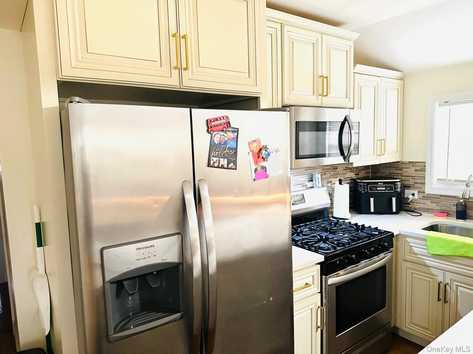 Kitchen featuring cream cabinetry, stainless steel appliances, backsplash, and light stone countertops Kitchen featuring cream cabinetry, stainless steel appliances, backsplash, and light stone countertops