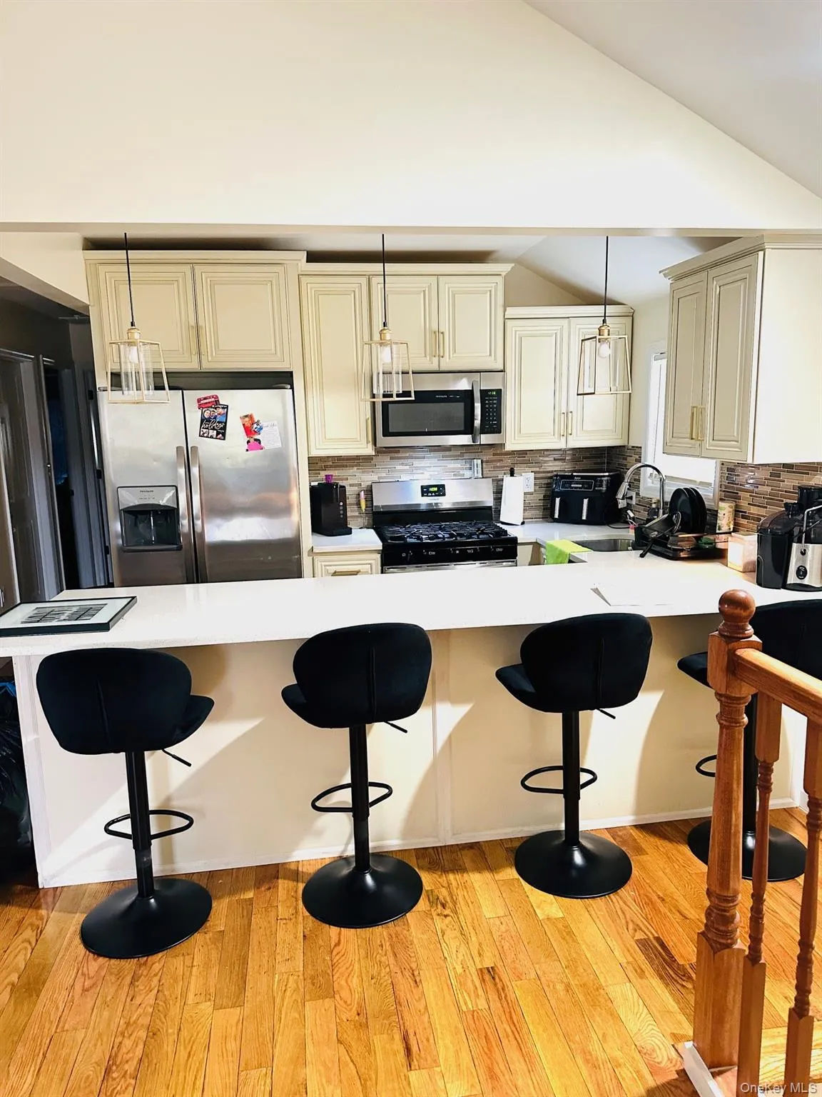 Kitchen with cream cabinetry, a breakfast bar area, hanging light fixtures, decorative backsplash, and lofted ceiling Kitchen with cream cabinetry, a breakfast bar area, hanging light fixtures, decorative backsplash, and lofted ceiling