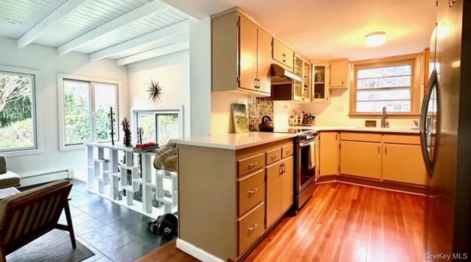 Kitchen featuring stainless steel appliances, light countertops, beam ceiling, healthy amount of natural light, and a baseboard heating unit Kitchen featuring stainless steel appliances, light countertops, beam ceiling, healthy amount of natural light, and a baseboard heating unit