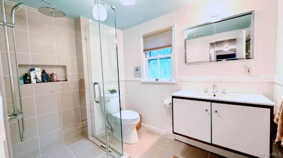 Bathroom featuring vanity, a shower stall, a wainscoted wall, and light tile patterned floors Bathroom featuring vanity, a shower stall, a wainscoted wall, and light tile patterned floors