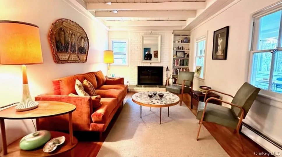 Living area with wood finished floors, a wooden ceiling with exposed beams, a brick fireplace, and baseboard heating Living area with wood finished floors, a wooden ceiling with exposed beams, a brick fireplace, and baseboard heating
