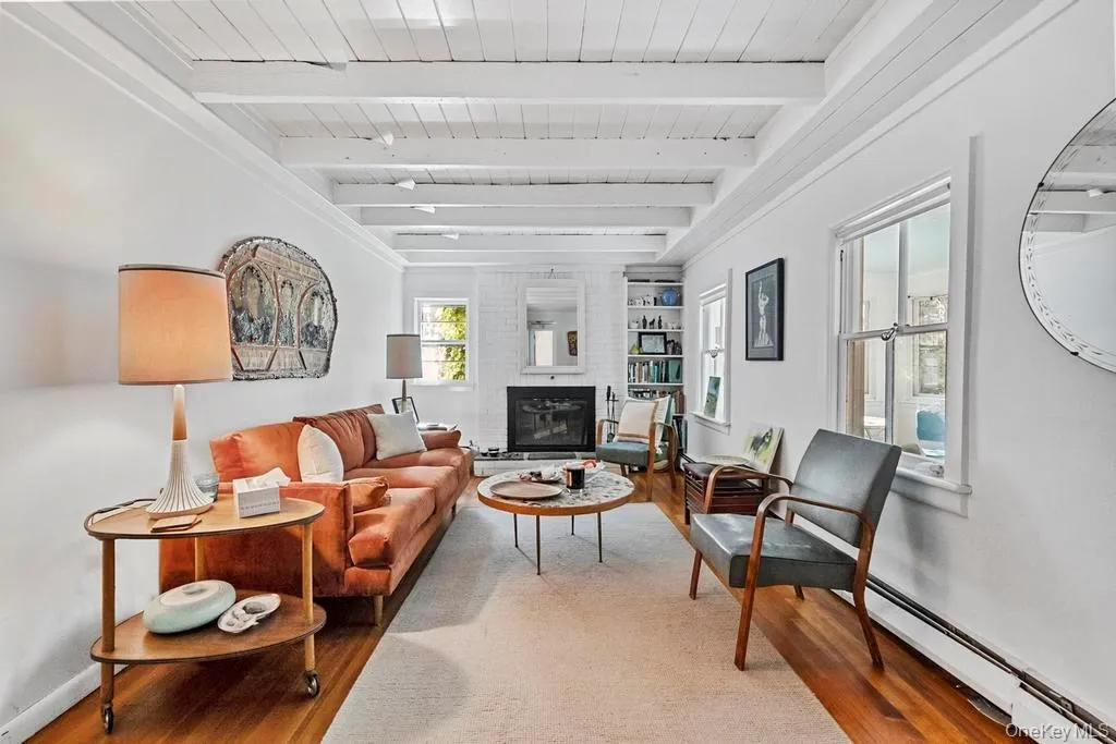 Living room with a baseboard radiator, wood finished floors, a large fireplace, and a wooden ceiling with exposed beams Living room with a baseboard radiator, wood finished floors, a large fireplace, and a wooden ceiling with exposed beams
