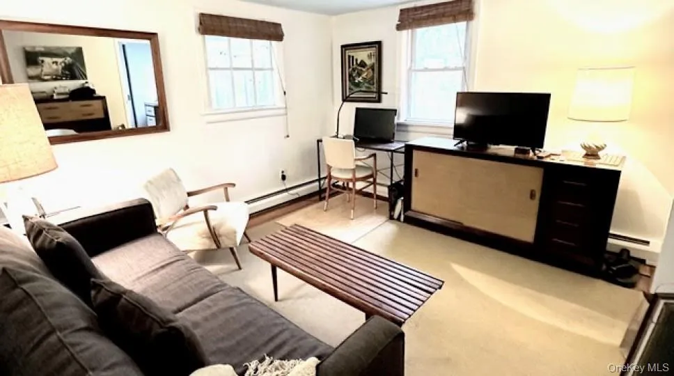 Living area with a desk, a baseboard heating unit, baseboard heating, and light colored carpet Living area with a desk, a baseboard heating unit, baseboard heating, and light colored carpet