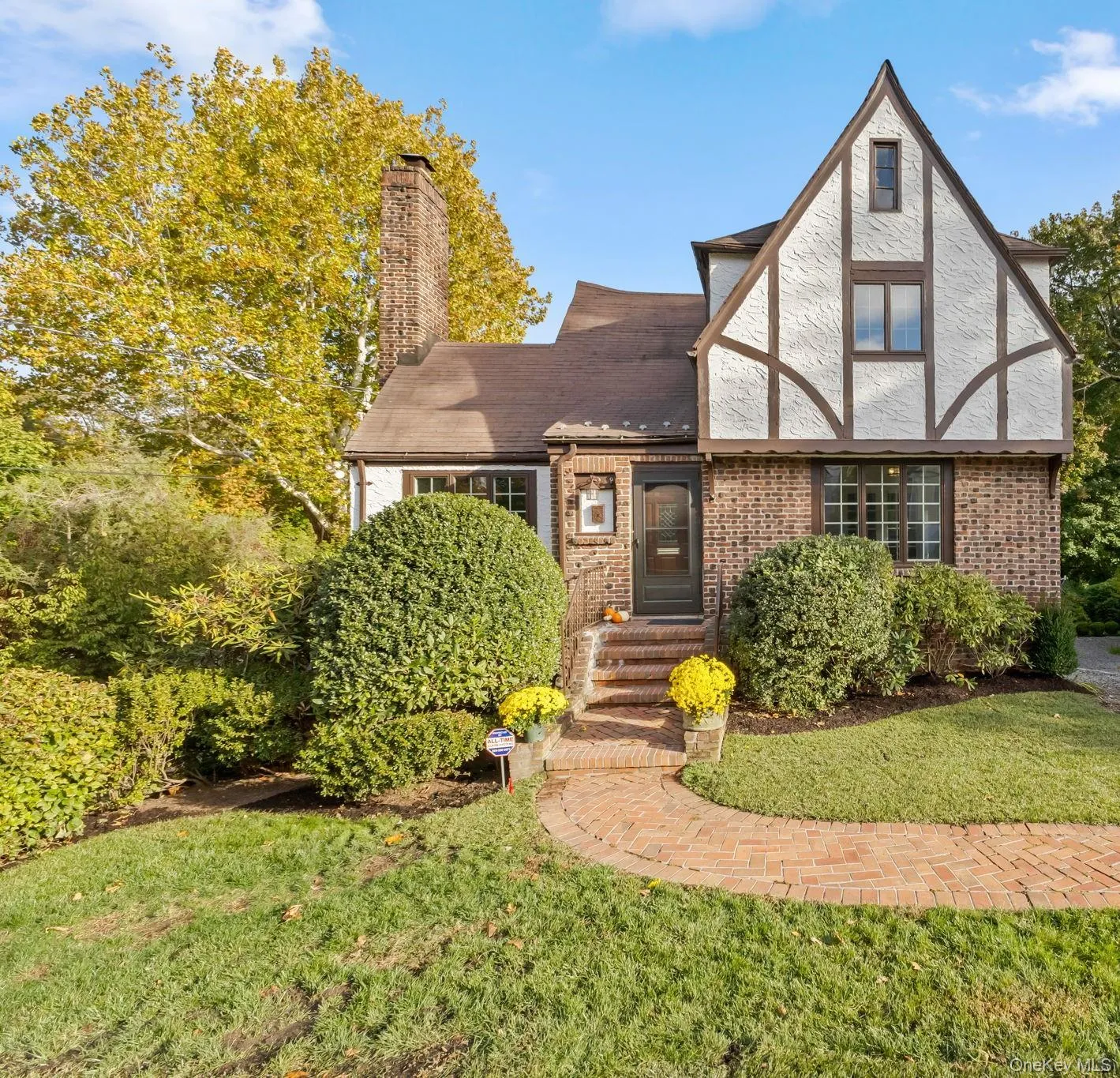 Tudor-style house with brick siding, a front lawn, and a chimney Tudor-style house with brick siding, a front lawn, and a chimney