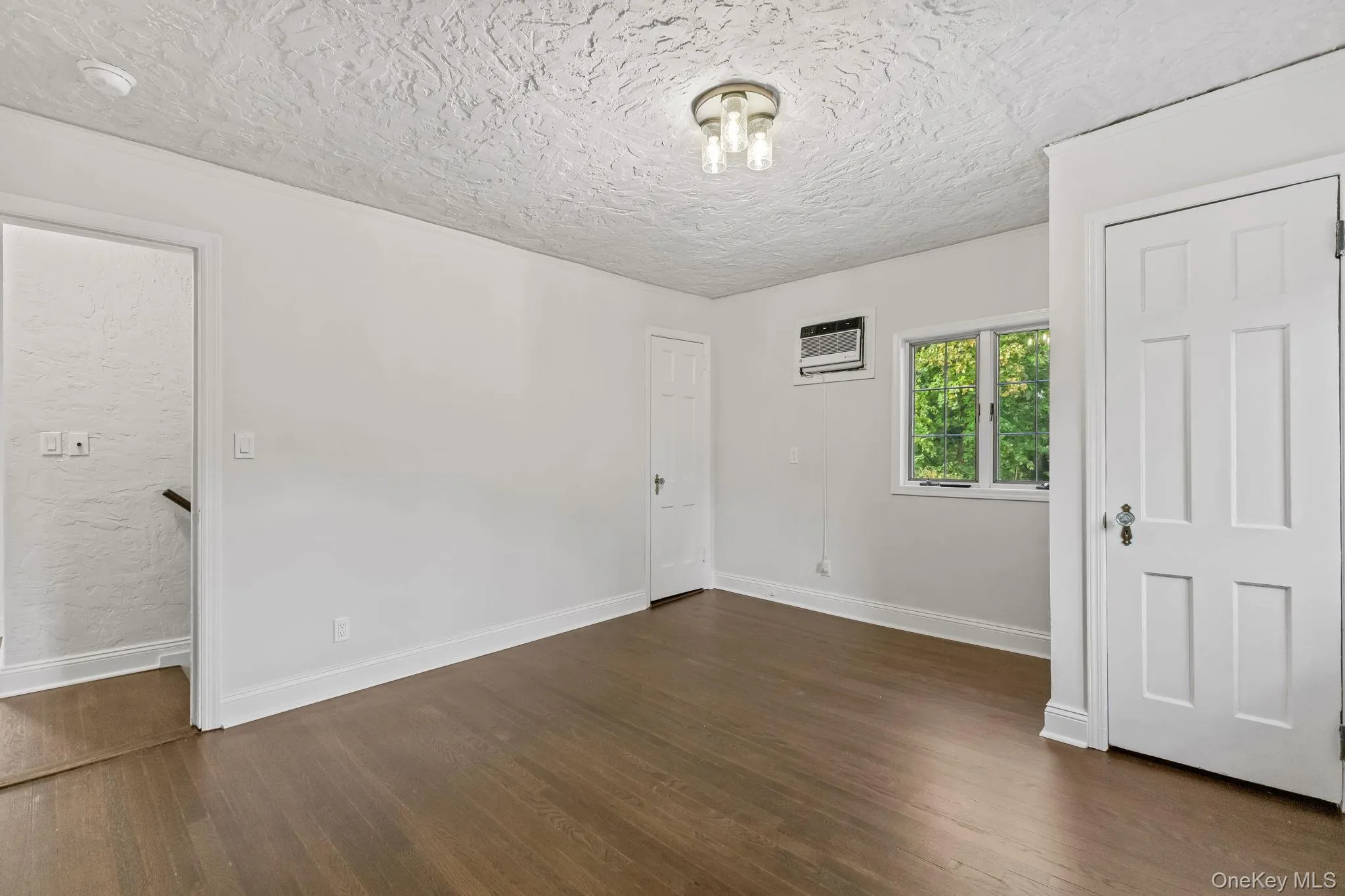 Unfurnished bedroom featuring dark wood-style floors, a textured ceiling, and an AC wall unit Unfurnished bedroom featuring dark wood-style floors, a textured ceiling, and an AC wall unit