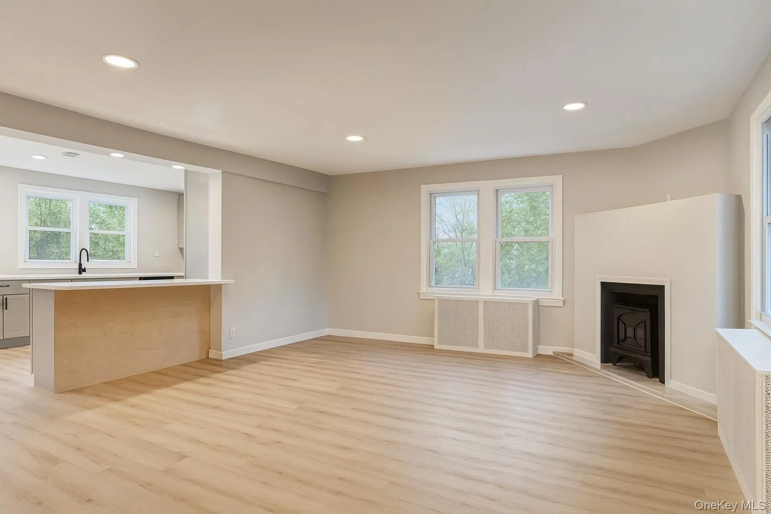 Unfurnished living room featuring radiator heating unit, recessed lighting, light wood-type flooring, and a fireplace Unfurnished living room featuring radiator heating unit, recessed lighting, light wood-type flooring, and a fireplace