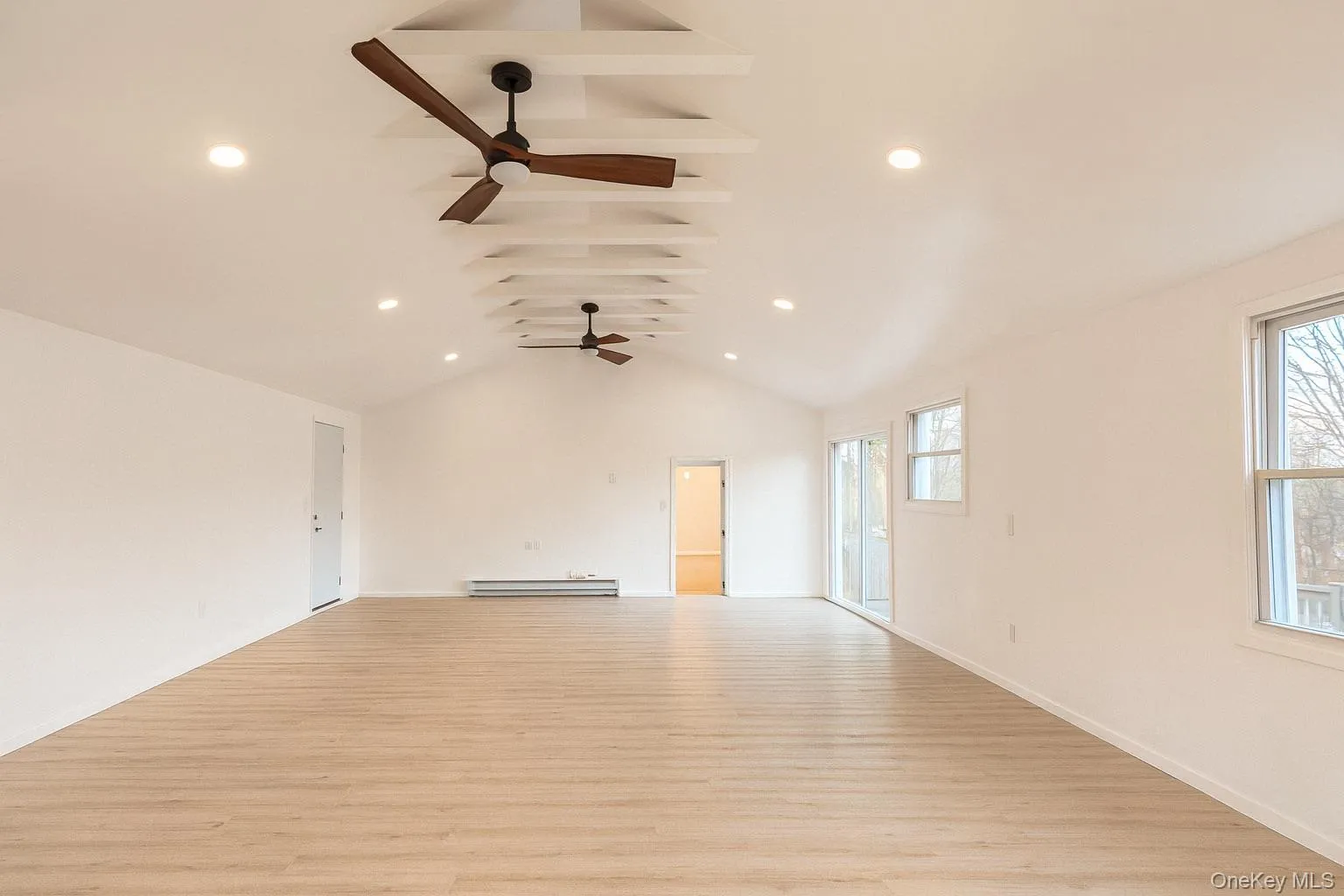Unfurnished living room featuring vaulted ceiling, light wood-type flooring, recessed lighting, and a baseboard radiator Unfurnished living room featuring vaulted ceiling, light wood-type flooring, recessed lighting, and a baseboard radiator