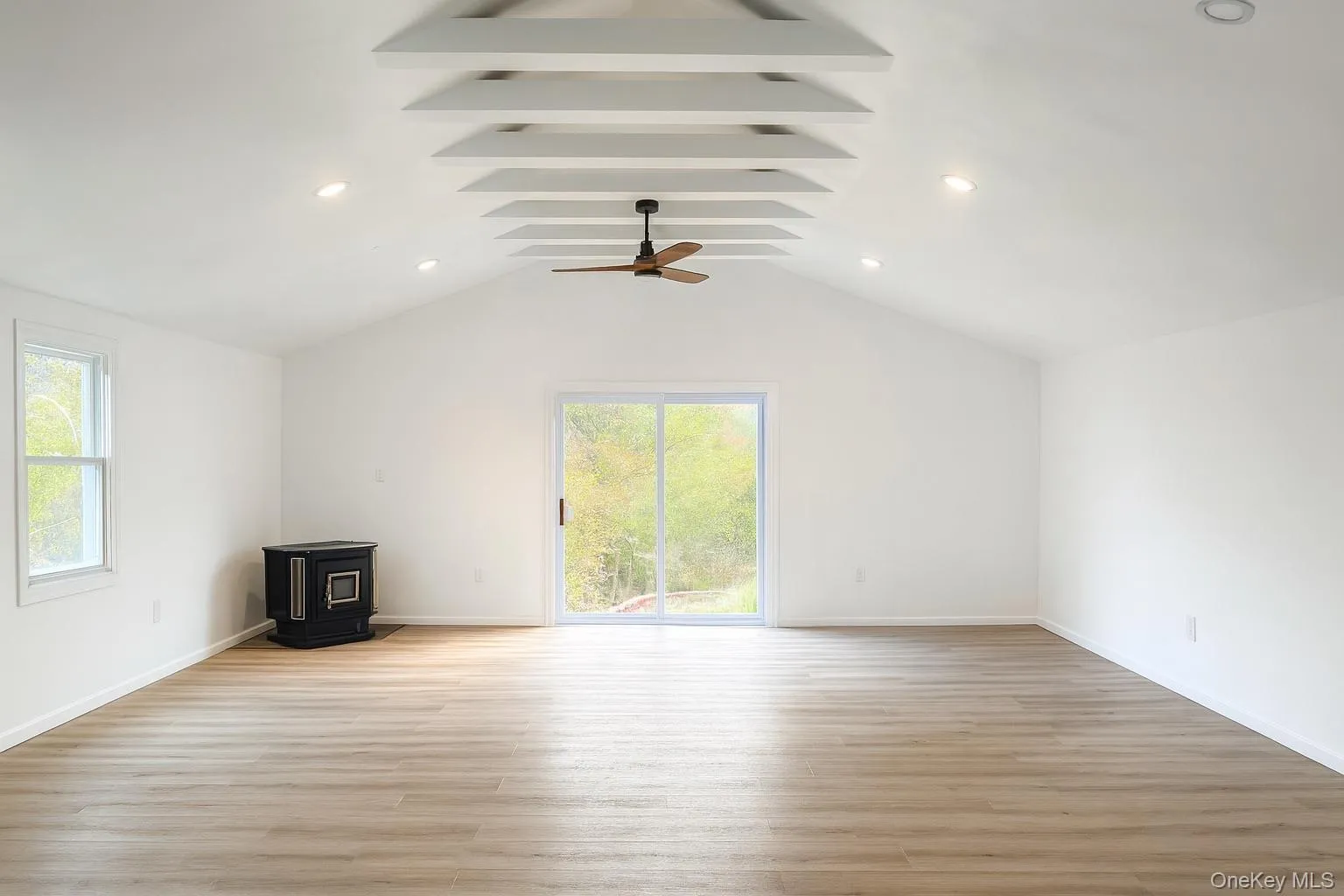 Unfurnished living room featuring a wood stove, healthy amount of natural light, lofted ceiling, light wood finished floors, and recessed lighting Unfurnished living room featuring a wood stove, healthy amount of natural light, lofted ceiling, light wood finished floors, and recessed lighting