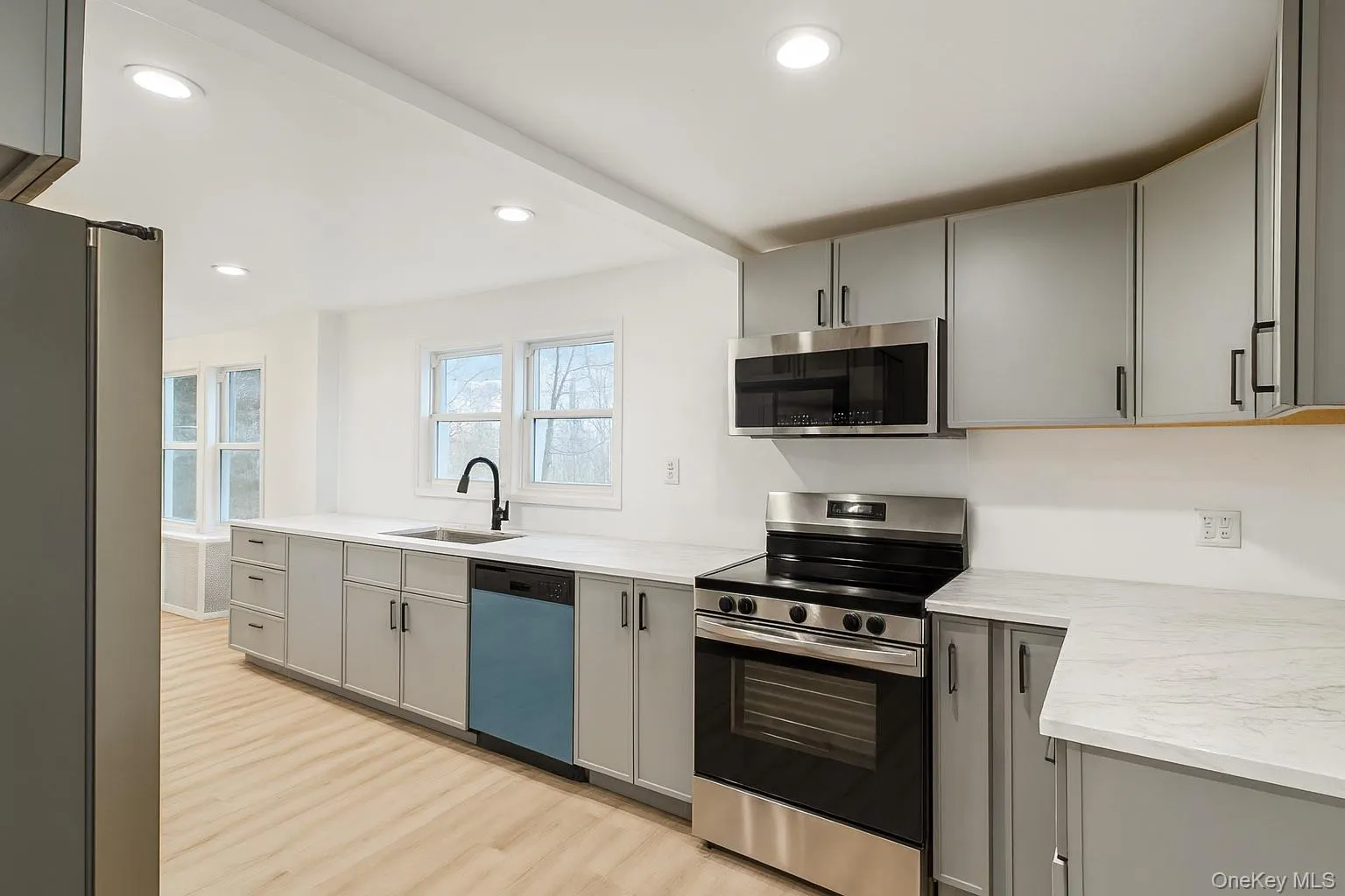 Kitchen with gray cabinets, appliances with stainless steel finishes, light wood-style flooring, recessed lighting, and light stone counters Kitchen with gray cabinets, appliances with stainless steel finishes, light wood-style flooring, recessed lighting, and light stone counters