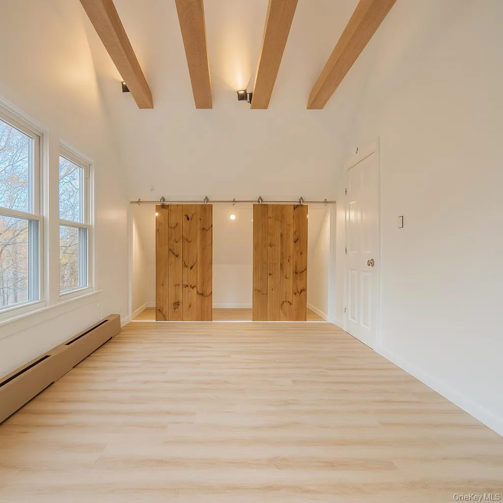 Top level room with baseboard heating, beamed ceiling, wood finished floors, a barn door, and high vaulted ceiling Top level room with baseboard heating, beamed ceiling, wood finished floors, a barn door, and high vaulted ceiling