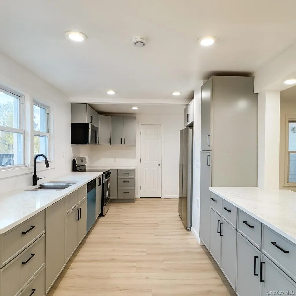 Kitchen with gray cabinets, recessed lighting, appliances with stainless steel finishes, light wood-type flooring, and light stone counters Kitchen with gray cabinets, recessed lighting, appliances with stainless steel finishes, light wood-type flooring, and light stone counters