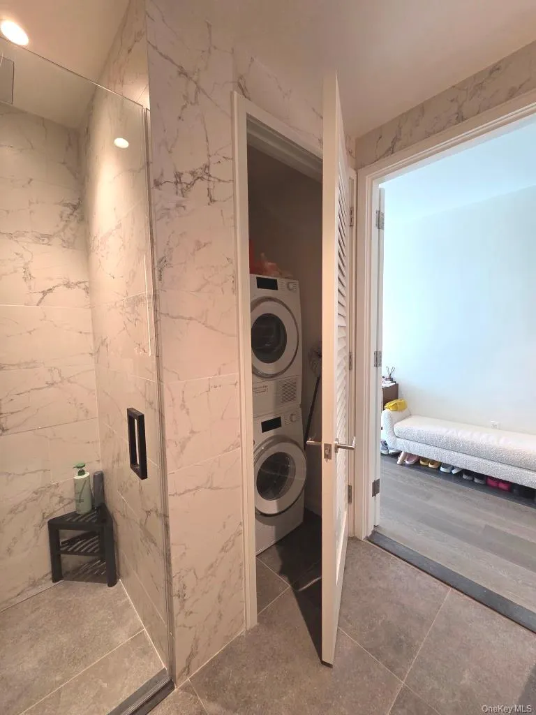 Bathroom with stacked washer / dryer, tile walls, tile patterned flooring, and connected bathroom Bathroom with stacked washer / dryer, tile walls, tile patterned flooring, and connected bathroom
