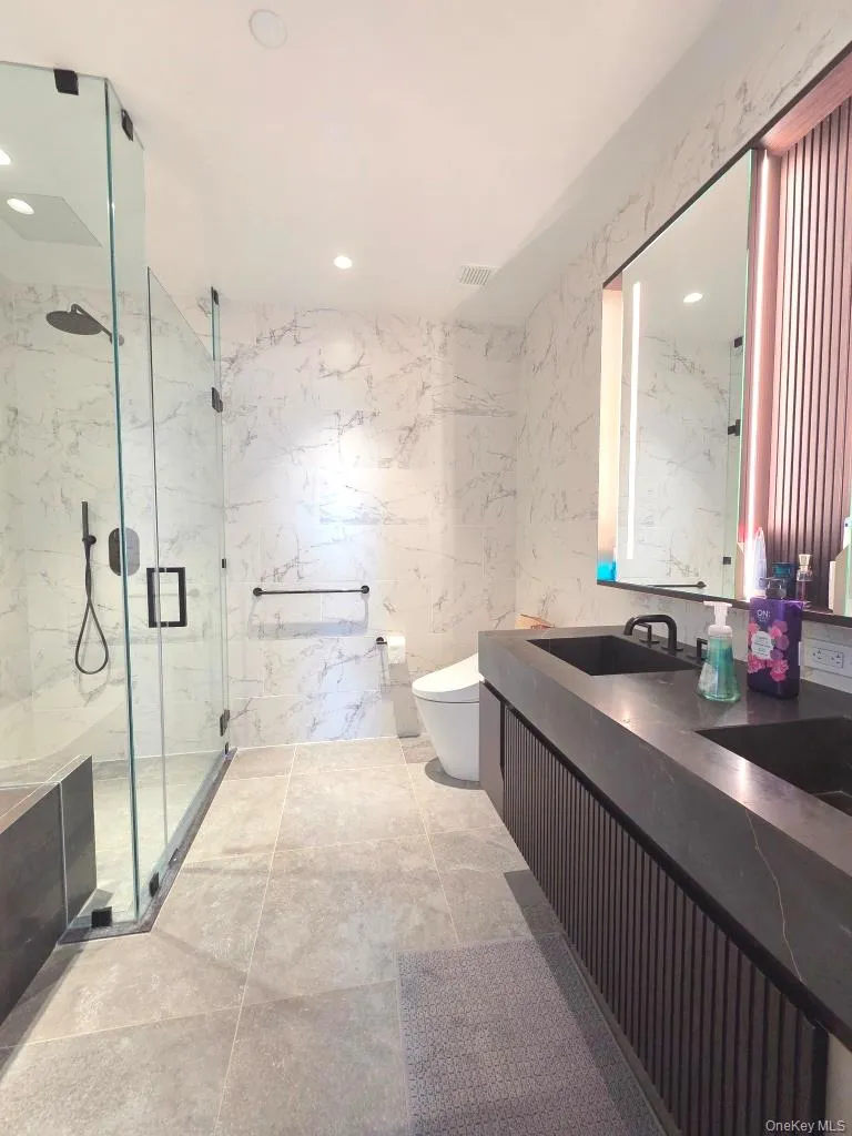 Full bathroom with tile walls, vanity, a marble finish shower, and recessed lighting Full bathroom with tile walls, vanity, a marble finish shower, and recessed lighting
