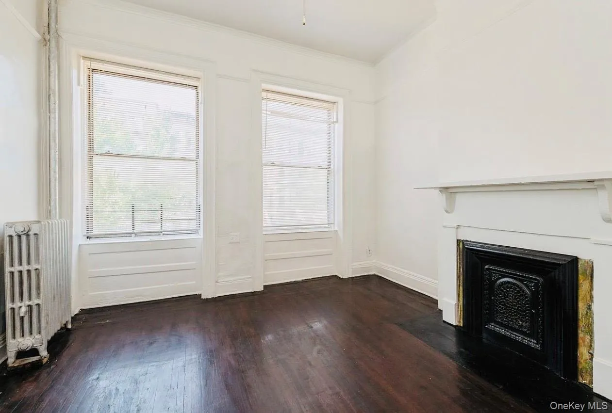 Unfurnished living room with radiator, dark wood-style floors, a fireplace, and crown molding Unfurnished living room with radiator, dark wood-style floors, a fireplace, and crown molding