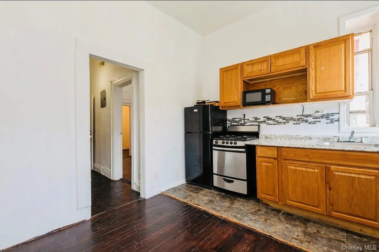 Kitchen with brown cabinetry, black appliances, tasteful backsplash, dark wood finished floors, and light stone countertops Kitchen with brown cabinetry, black appliances, tasteful backsplash, dark wood finished floors, and light stone countertops