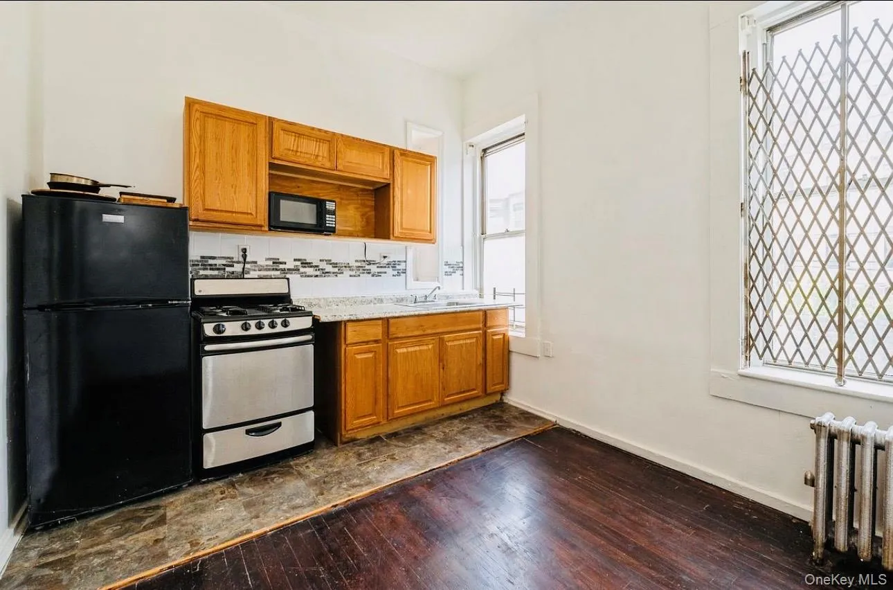 Kitchen with black appliances, brown cabinetry, decorative backsplash, light countertops, and radiator heating unit Kitchen with black appliances, brown cabinetry, decorative backsplash, light countertops, and radiator heating unit
