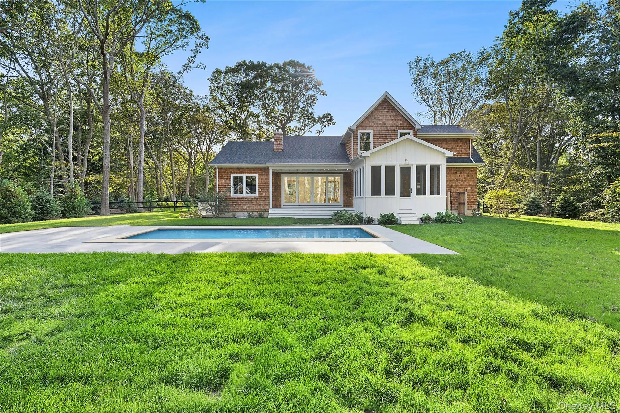 Back of property featuring a sunroom, a chimney, a patio area, an outdoor pool, and a shingled roof Back of property featuring a sunroom, a chimney, a patio area, an outdoor pool, and a shingled roof