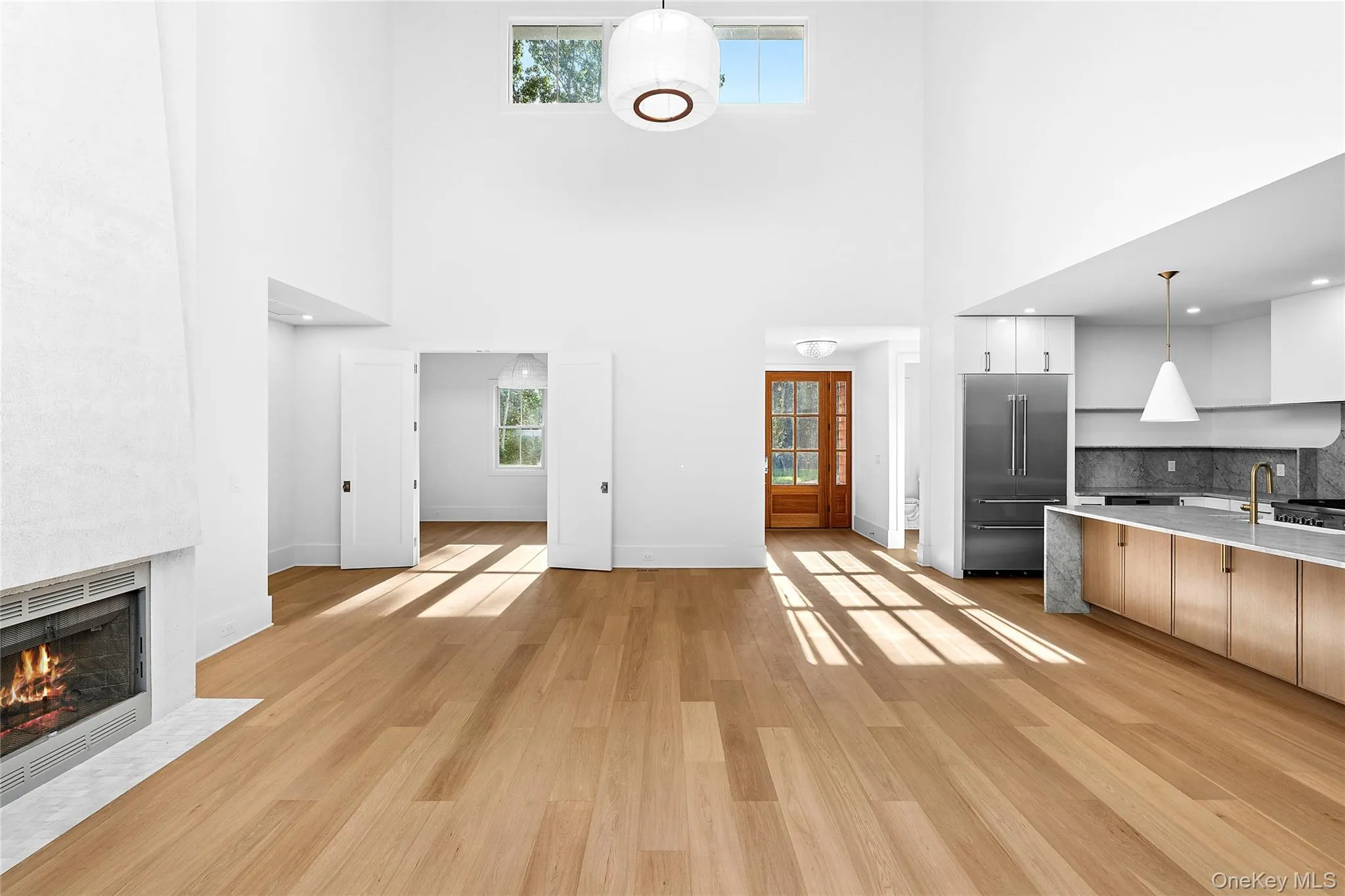 Unfurnished living room featuring a high ceiling, light wood finished floors, and a large fireplace Unfurnished living room featuring a high ceiling, light wood finished floors, and a large fireplace