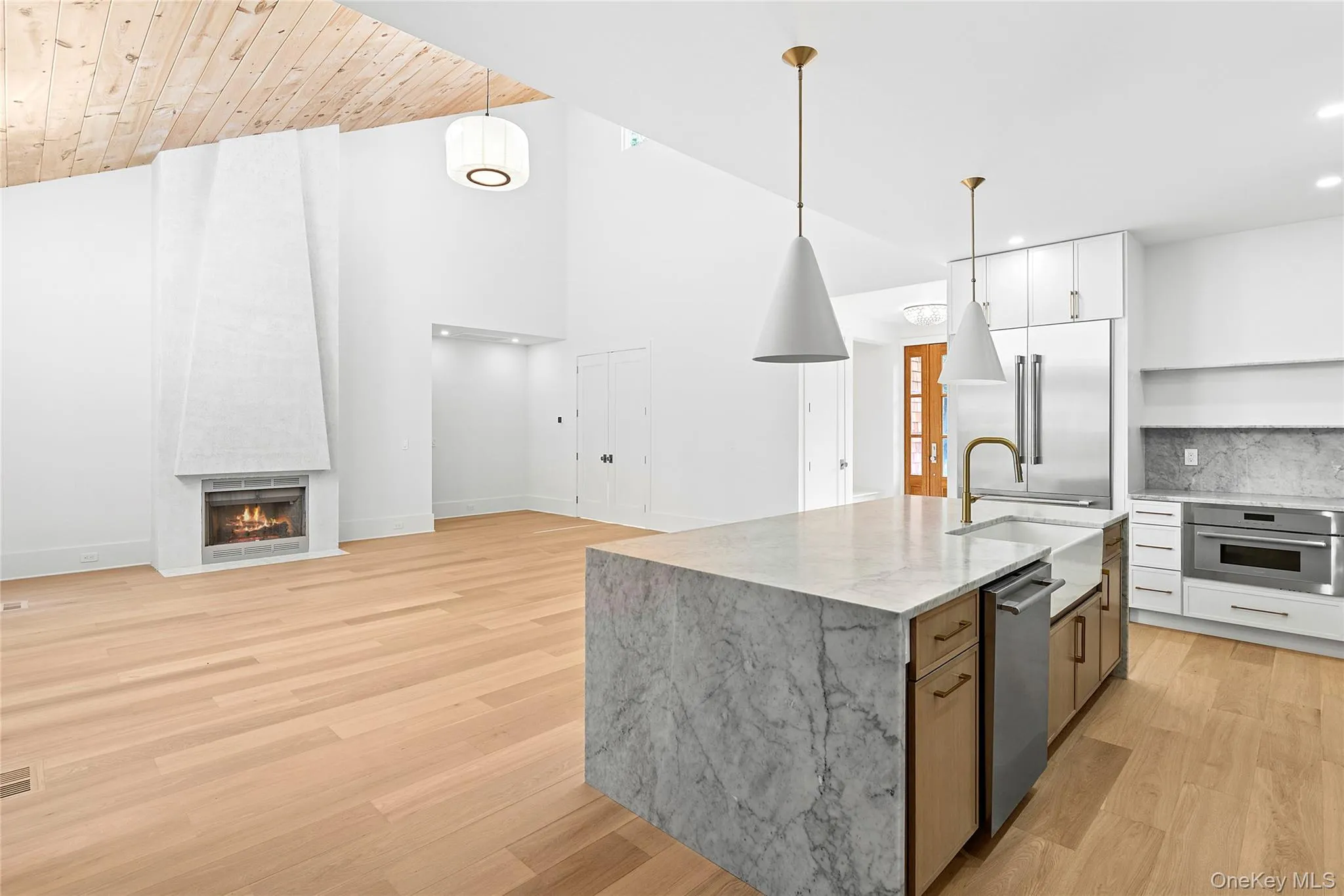 Kitchen with open floor plan, light Carera marble countertops, white cabinets, light wood-style flooring, and high vaulted ceiling Kitchen with open floor plan, light Carera marble countertops, white cabinets, light wood-style flooring, and high vaulted ceiling