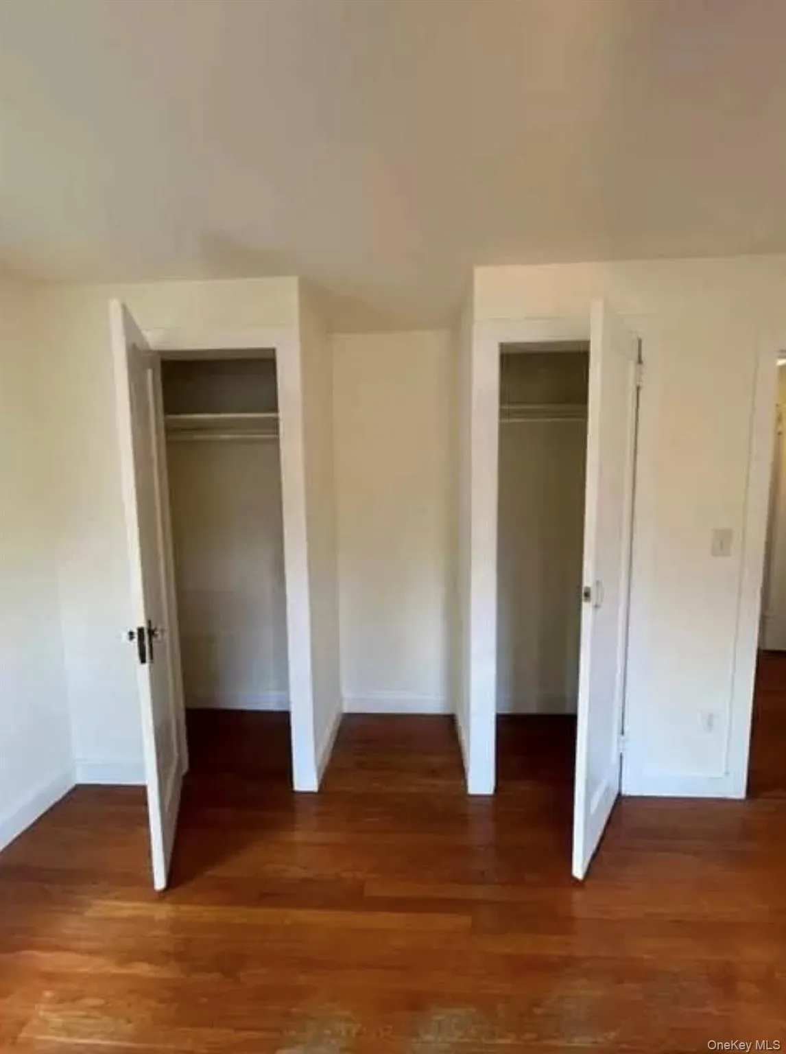 Unfurnished bedroom with multiple closets and dark wood finished floors Unfurnished bedroom with multiple closets and dark wood finished floors